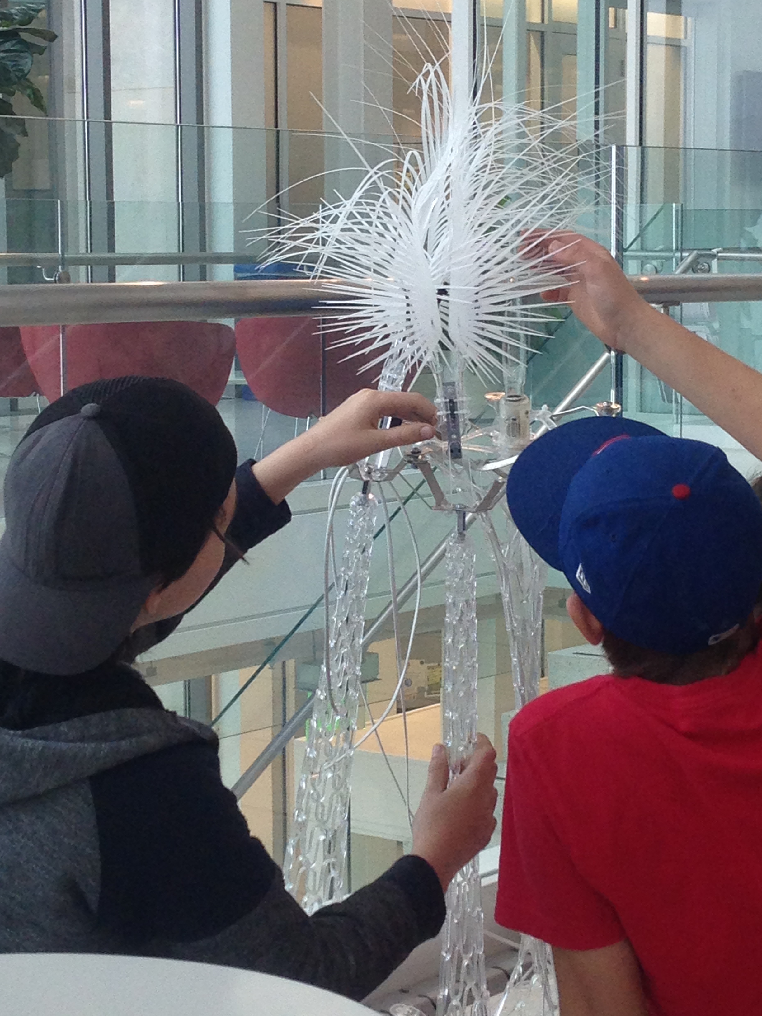 Two children interacting with, and looking closely at part of a sculpture that is designed to respond to humans through a series of sensors.